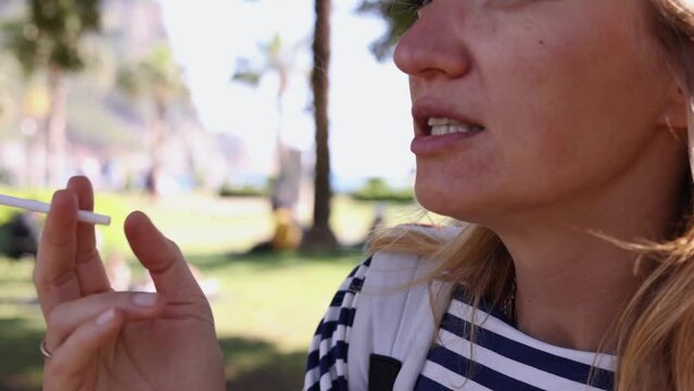 Close up of woman holding cigarette in hand, unhealthy stressed woman smokes cigarette in summer park