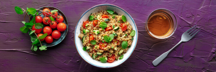 Quinoa tabbouleh salad in a bowl panorama, a healthy dinner with tomatoes and mint, overhead flat lay shot with a drink on a purple background