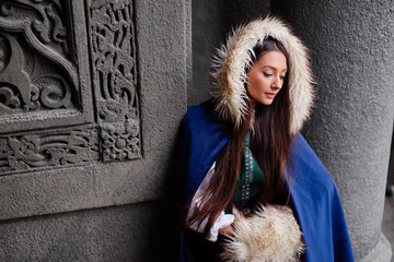 Fairytale princess wearing cloak with medieval castle wall on the background.