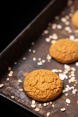 Craft and rustic four oatmeal cookies. Dark food aesthetics, black background with several oat flakes.