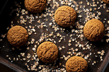 Craft and rustic four oatmeal cookies. Dark food aesthetics, black background with several oat flakes.