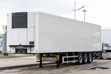 A new white refrigerated semi-trailer in the parking lot, waiting to be loaded with cargo. Freight...