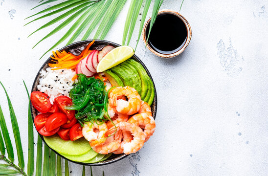 Poke bowl with shrimp, avocado, radish, carrot, tomato, seaweed and white rice. White table background, top view