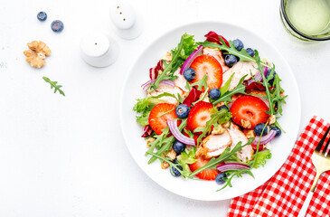 Summer strawberry and grilled chicken healthy salad with arugula, blueberries, red onion and walnuts, white table. Fresh useful dish for healthy eating