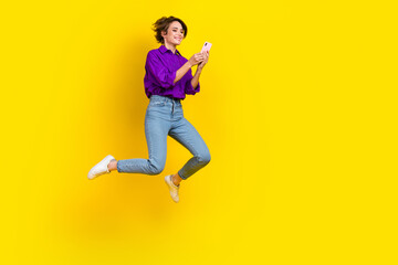 Fototapeta na wymiar Full length photo of sweet cute lady wear violet shirt jumping chatting samsung iphone apple device isolated yellow color background