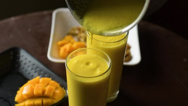 A lady putting mango slices and chopped nuts on top of mango lassi or mango yogurt smoothie a tasty popular drink in India.