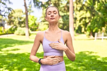 In the park, a woman in sportswear finds serenity through diaphragmatic breaths.