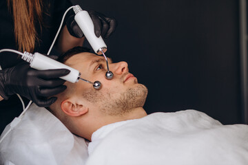 Young man undergoing microcurrent therapy in beauty salon