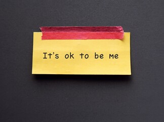 Yellow note stick on blue background with text 'It’s ok to be me' concept of using positive...