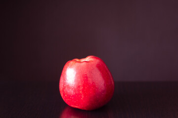 Fototapeta na wymiar A red apple lies on a table against a dark background. Light from the window