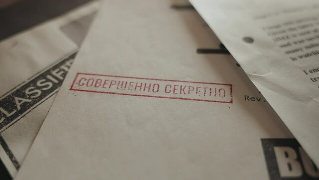 Hand marking paper as Top Secret in Russian language using red ink stamp. Official document labeled with rubber stamp translating to highly confidential or top secret. Retro-looking classified paper