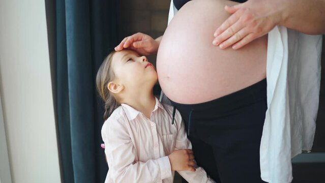 Cute little girl 4s hugging pregnant mom belly. The child touches the belly of the pregnant woman.