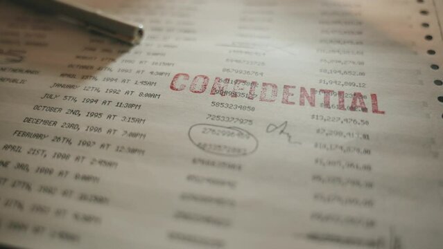 Paper with bank numbers and accounting information is stamped as confidential. Red ink rubber stamp marks retro looking document with money transfers and sensitive information as confidentail