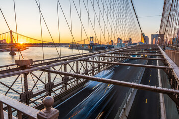 A rising sun about the Manhattan Bridge and the Brooklyn Bridge full of traffic.