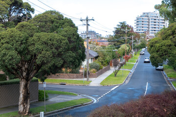 Elevated view of a quiet suburban street with trees, Australian homes and modern apartment buildings in the distance. Beautiful neighborhood environment in Melbourne VIC Australia.