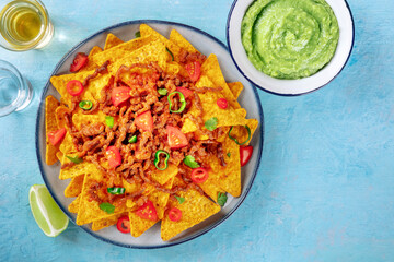 Nachos, Mexican food, tortilla chips with beef and fresh vegetables, overhead flat lay shot with tequila, limes, and guacamole, with copy space