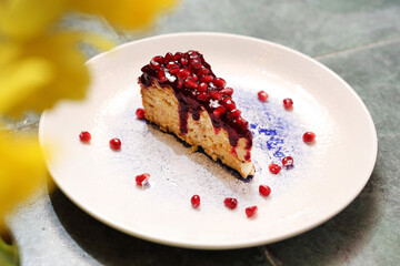 A piece of cheesecake with fruit glaze, decorated with pomegranate seeds, on a white plate, selective focus, top view. 