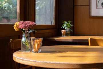 Background texture of a window side wooden table with flower vase and sugar sachets in warm natural sunlight in a cafe. Copy space for your   Food or drink product design.