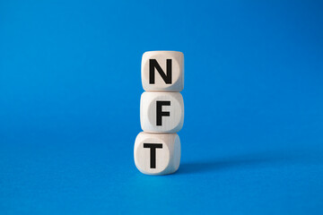 NFT - non-fungible token symbol. Concept word NFT on wooden cubes. Beautiful blue background. Business and NFT concept. Copy space.