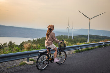 Woman wearing cute outfit riding bicycle at sunset with wind turbine mountains and rivers in the background