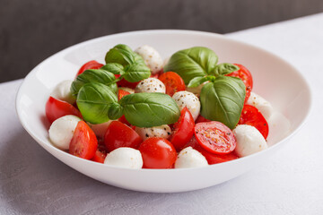 A view of caprese salad with tomato, mozzarella, basil and olive oil on white plate. Isometric style. Mediterranean cuisine. Focusing on the basil leaves on top.
