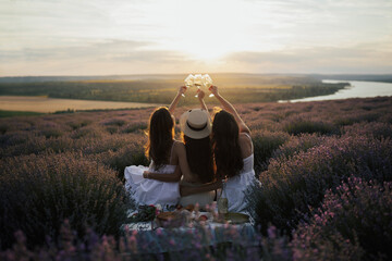 Young women enjoying view of sunset in the lavender field. They clinking glasses of wine to...