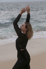 Portrait of young woman in black outfit on isloated empty ocean beach, concept of freedom and off the map travel