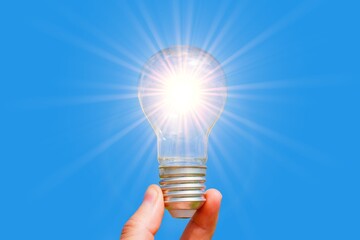 Glowing Light Bulb in Hand Against Blue Background