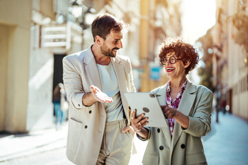 Fototapeta premium Business people outdoors. Handsome business man and his beautiful female colleague discussing new project while crossing the street, urban background. 