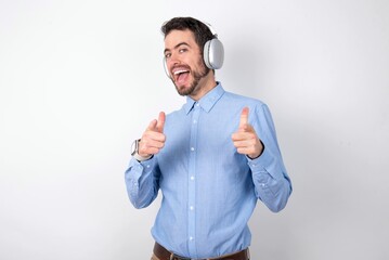 businessman wearing blue t-shirt with headphones over white background directs fingers at camera...