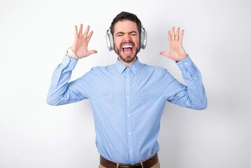 businessman wearing blue t-shirt with headphones over white background goes crazy as head goes...