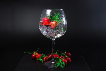 A glass of cocktail with strawberries and mint on a black background. refreshing drink
