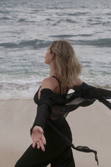 Portrait of young woman in black outfit on isloated empty ocean beach, concept of freedom and off the map travel