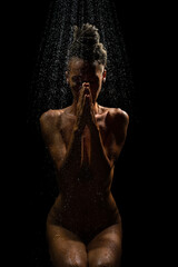Artistic view of woman praing under  falling rain against black background.