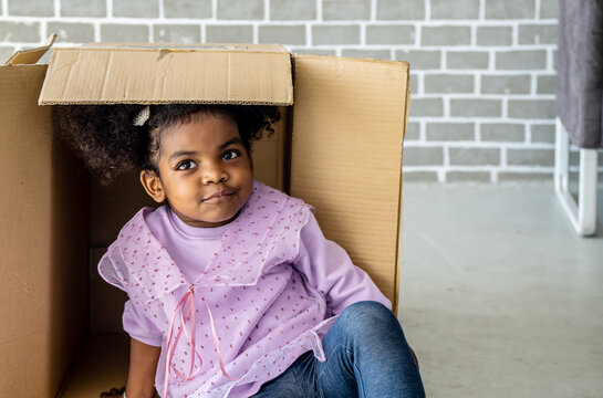 African american cute baby girl enjoy playing with cardboard box at home