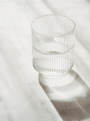Glass with clean clear water and shadows stands on a white table
