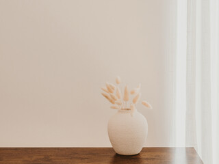 White ceramic vase with dried flowers on brown wood table.