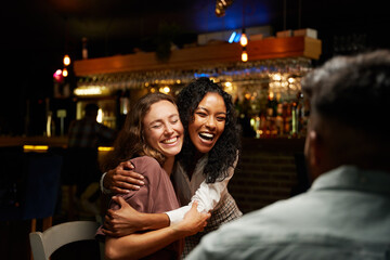 Happy young multiracial group of friends in casual clothing hugging at restaurant