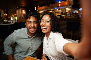 Young multiracial couple in casual clothing smiling while taking selfie with mobile phone at bar