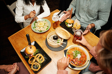 Young multiracial group of friends in casual clothing sitting with beer and dinner at restaurant