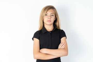 Fototapeta premium Serious pensive beautiful teen girl wearing black dress over white studio background feel like cool confident entrepreneur cross hands.