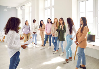 Fototapeta premium Speaker giving interactive motivational speech at business workshop. Smiling motivated female participants talking together at corporate meeting, staff training. Life coaching, team building