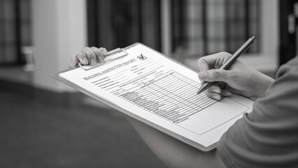 An engineer hand is using a pen checking on the building inspection report form to QC building...