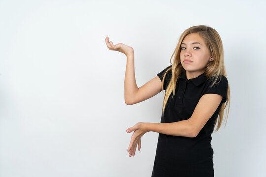 beautiful teen girl wearing black dress over white studio background pointing aside with both hands showing something strange and saying: I don't know what is this. Advertisement concept.