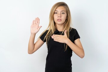 beautiful teen girl wearing black dress over white studio background Swearing with hand on chest...