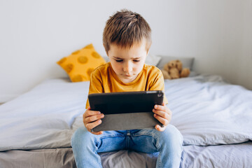 Toddler boy playing with digital wireless tablet computer at home. Baby child growing with online applications. Child and electronic devices concept. Portrait of toddler with smartphone