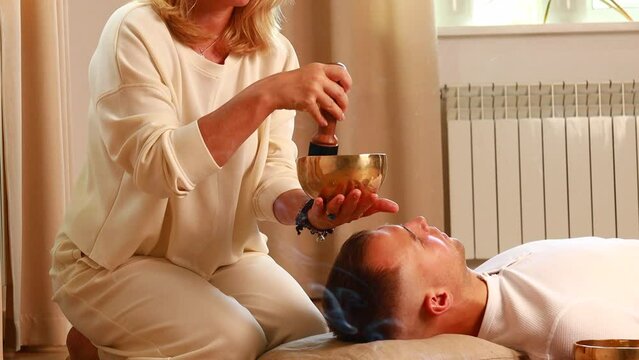 Woman playing on a tibetian singing bowl maling massage meditation for a man