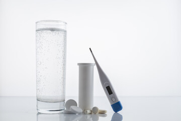 Pack of pills and capsules glass of water and a thermometer on a white background with space for text