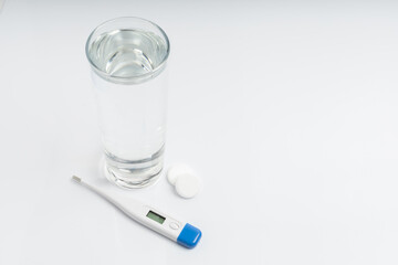Pack of pills and capsules glass of water and a thermometer on a white background with space for text