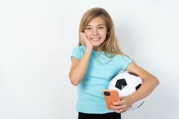 Joyous beautiful caucasian teen girl wearing sportswear  poses with mobile phone device, types text message on modern smartphone, watches funny video during free time, enjoys good internet connection,